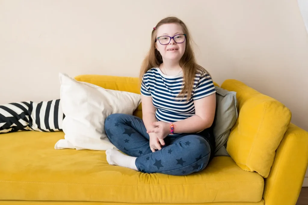 Disabled girl with down syndrome sitting on Yellow couch and smiling at camera